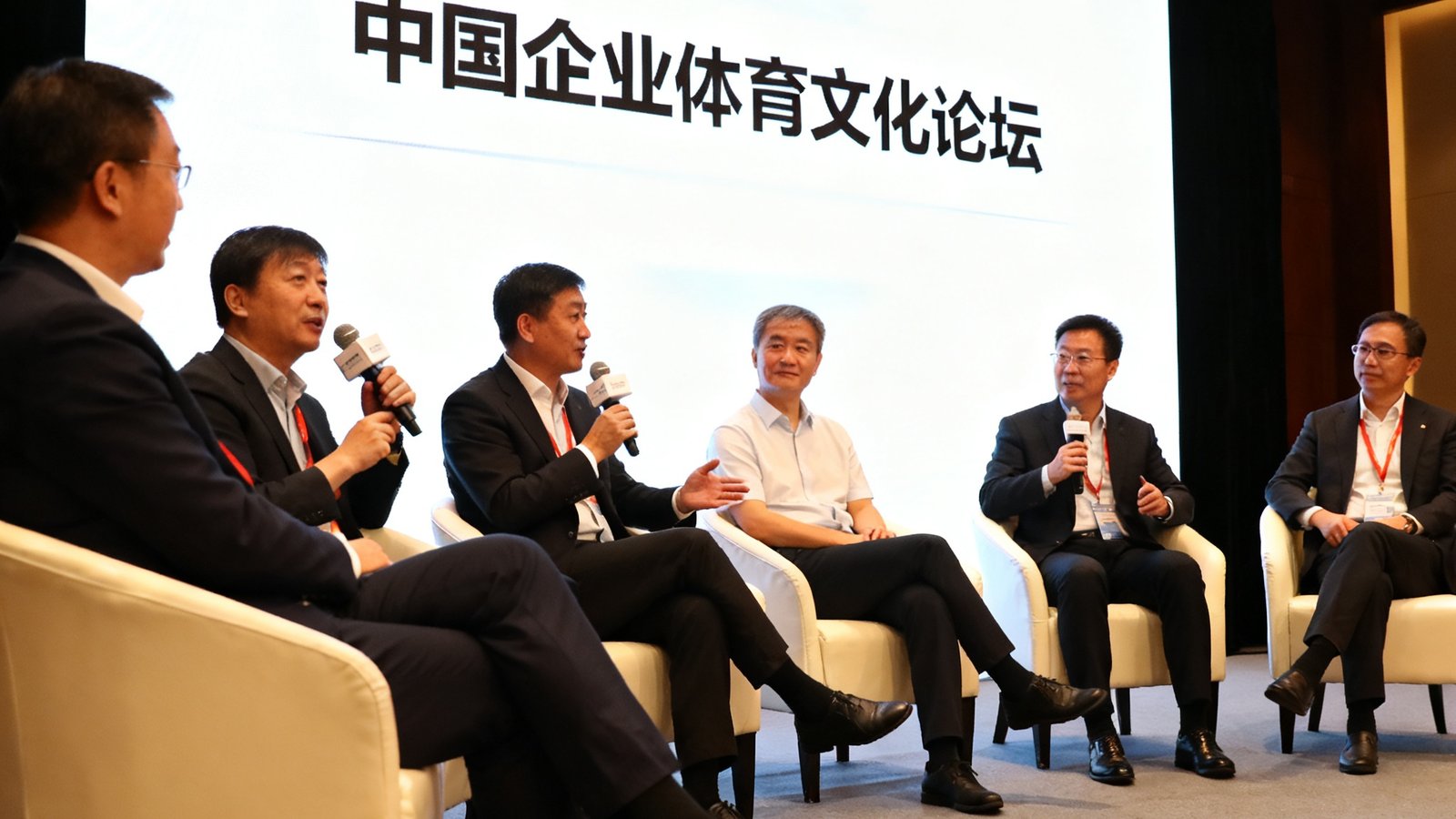 中国企业体育文化论坛圆桌讨论现场，多位嘉宾在台上交流，背景屏幕显示论坛主题